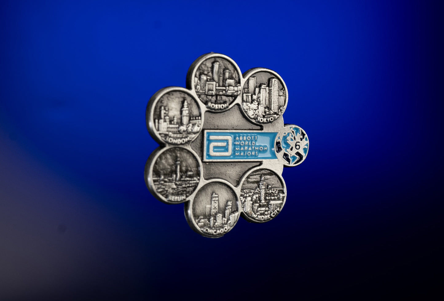 Abbott World Marathon Majors Six Star pin badge featuring raised city skyline icons for Tokyo, Boston, London, Berlin, Chicago, and New York, shown on a blue gradient background